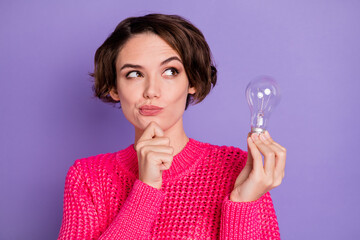 Photo of young girl think deep creative look empty space hand touch chin hold light bulb isolated over purple color background