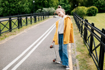 Happy teenage girl learning to ride a skateboard in the city park.