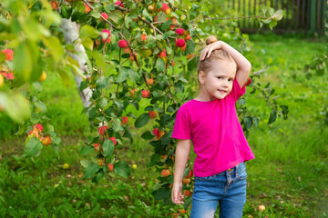 Portrait of children in an apple orchard. Little girl in pink Tshirt and denim skirt on background of apple tree branches. Carefree childhood, happy child