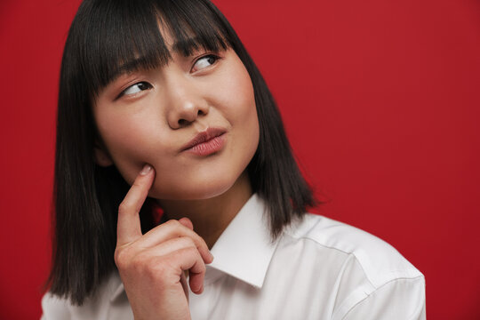 Young asian woman pointing finger at her cheek and looking aside