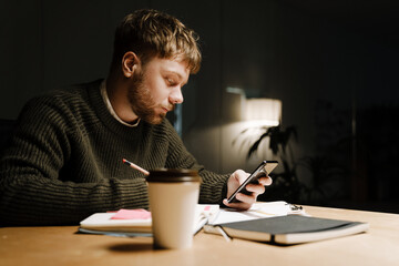 Young ginger man using mobile phone while working in office