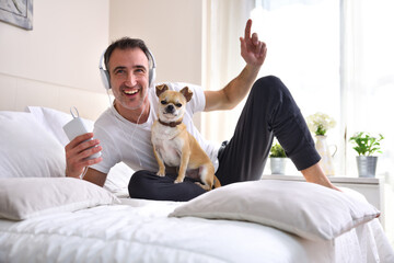 Laughing man listening music lying in bed with chihuahua