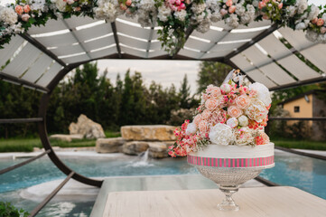 Wedding cake with flowers decoration and a swimming pool on background.