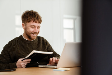 Young ginger man working with laptop while sitting at table in office