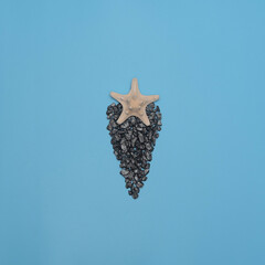Starfish on small dark stones on blue background. Summer time, minimalism concept. Flat lay style with copy space 