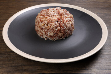 Nasi dagang special brown white rice cooked with coconut milk and spice on black off white rim plate on rustic dark wooden background