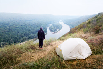 A tourist stands near a tent on the top of a mountain