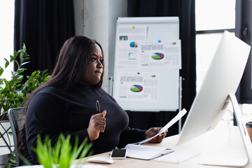 african american plus size businesswoman looking at computer monitor in office.