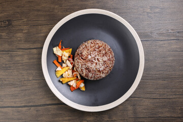 Nasi dagang special brown white rice cooked with coconut milk pickled fruit vegetable pineapple carrot on black offwhite rim plate over rustic dark wooden background