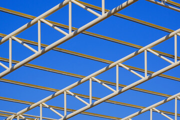 Fototapeta premium Low angle and diagonal view of yellow metal building roof structure in construction area against blue sky background