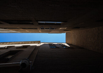 Looking up to blue sky trapped alone between two tall high rise buildings in dark alley way.