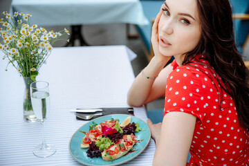 Beautiful young woman having dinner at cafe, looking at camera. Cropped close up top view portrait of beatiful charming girl in red dress