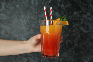 Female hand holds Tequila sunrise cocktail on black smokey background