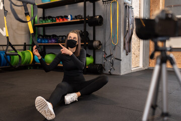 Fototapeta na wymiar Athletic fitness instructor with a protective mask, gym dumbbell, and balance gym workout exercises live on camera for sportive followers on social media. Home fitness workout class live streaming. 