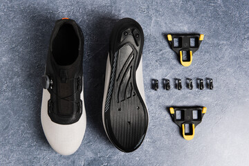 Road cycling shoes and disassembled cleats on a stone surface.