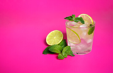 lemonade with mint and lime wedges on a pink background