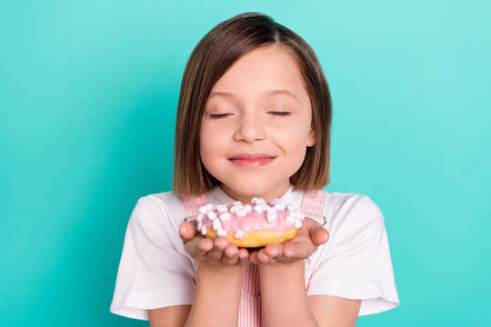 Photo of charming shiny schoolgirl dressed pink overall enjoying sweet donut smiling isolated turquoise color background