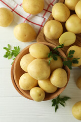 Wooden bowl with young potato on white wooden table