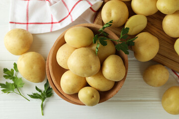 Wooden bowl with young potato on white wooden table