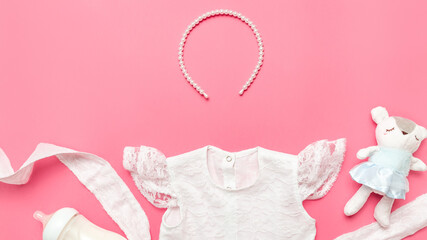 Stylish white baby dress and accessories on a pink background