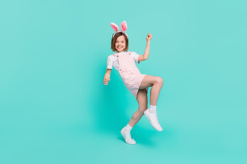 Photo of cute lucky schoolgirl dressed pink overall rabbit ears rising fists smiling isolated...