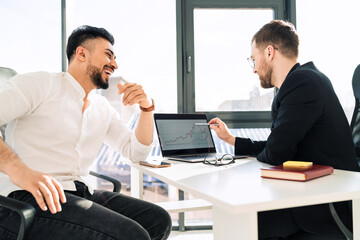 Two businessmen at laptop are watching chart of the company's income growth