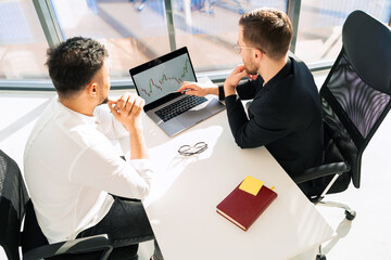 Two businessmen at laptop are watching chart of the company's income growth