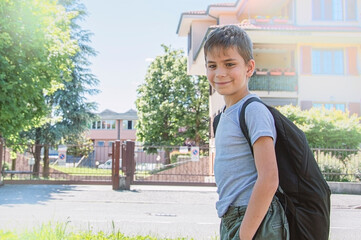 The schoolboy comes back to school. He has smile. Behind shoulders at the pupil a satchel.