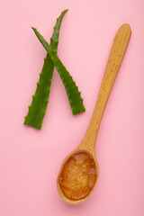 Aloe vera gel on wooden spoon with aloe vera on pink background.
