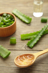 Aloe vera gel on wooden spoon with aloe vera and oil bottle on grey background. Vertical photo