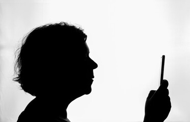 Black silhouette in profile, of woman consulting her smartphone, on white background, horizontally,...