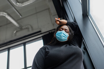 low angle view of african american plus size businesswoman in medical mask feeling unwell in office.