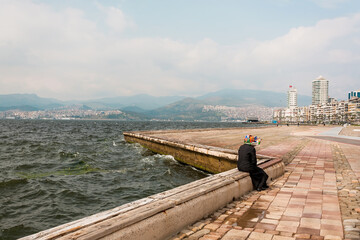 Woman alone siting on the seashore, on the embankment in the old Turkish city Izmir.
