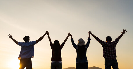 Group of happy friends are having fun with raised arms together in front of mountain and enjoy sunrise sunset showing unity and teamwork. Friendship happiness leisure partnership team concept.