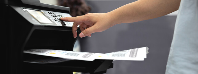 Bussiness man Hand press button on panel of printer, the printer is printing office documents....