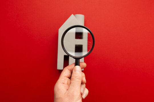 Housing inspection. A hand with a magnifying glass looks for flaws in a miniature house. Hidden defects in real estate.