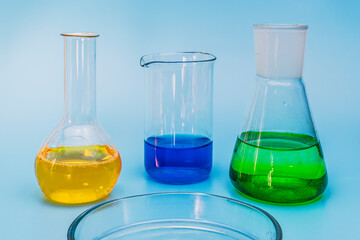 Three glass laboratory flasks with solutions of yellow, green and blue on a gentle blue medical background. The concept of medical and chemical experiments and research. Close-up. copy space.