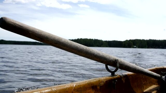 View from the side of the boat. Sailing about a lake on a sunny day past an island with a green forest. Oar shank in a boat