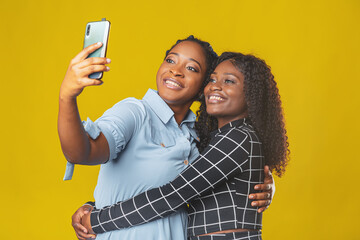 two friends african american girls take a selfie or video call with friends on a yellow background. video chat, video conference