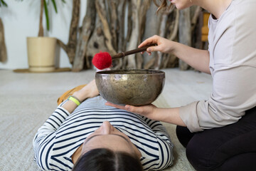 Caucasian masseuse perform tibet sound therapy at relaxed female. Young woman get singing bowls massage. Alternative treatment for mental health, energy recovery, harmony and reducing stress concept