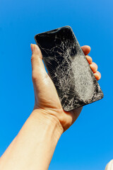 A black smartphone with a cracked screen from falling to the ground was in the hand of a young man...