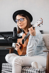 podcaster creates content, happy woman musician with guitar records podcast with microphone and headphones, Caucasian woman in glasses and hat, in recording studio records song or music, new album