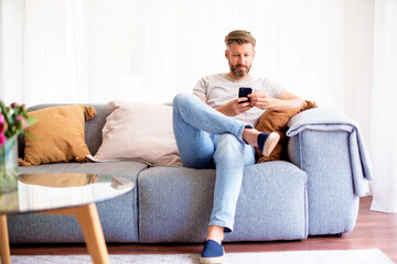 Fototapeta premium Handsome man wearing casual clothes while sitting on sofa and using his phone