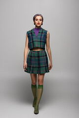 Fototapeta premium full length of young woman in headband and vintage checkered outfit posing on grey.