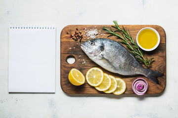 Dorado fish on a rustic wooden cutting board with spices and a notebook for recipe or menu.