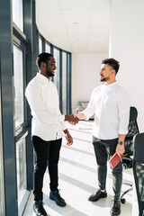 Two multiracial businessmen shake hands in office