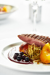 Grilled duck breast with peaches in berry sauce, grilled duck fillet on a white plate, close-up of...