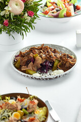 Sliced boiled beef tongue on a plate with fresh herbs and pickled cucumbers, light background