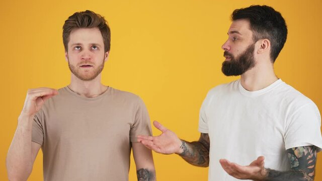 Two guys are talking while one of them is showing blablabla gesture standing isolated over yellow wall in the studio