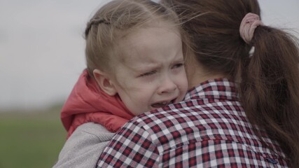 Mommy soothes baby. child is crying in park in arms of mom. family mother and child with tears in their eyes hugs their mother, emotionally. loving young mother hugs and soothes her little daughter